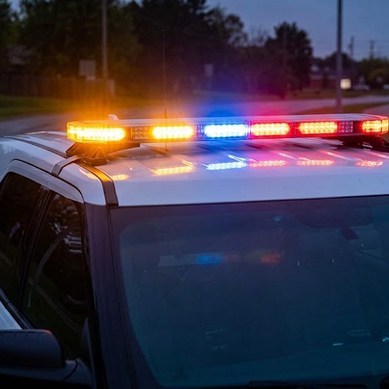 A first responder service vehicle is parked on the side of a wet road at dusk with its roof-mounted emergency LED light bar brightly illuminated